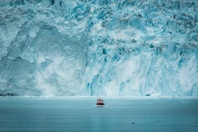 A small passenger boat in front of the huge glacier wall at the Eqi glacier in Greenland - Photographer: Mads Pihl - Visit Greenland